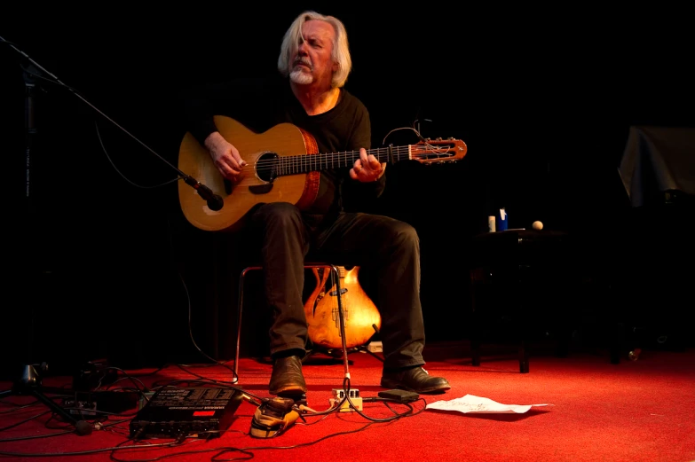 the man is sitting on stage playing a guitar