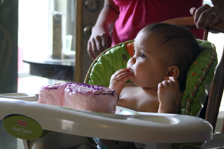 the child is sitting in her high chair with the cake