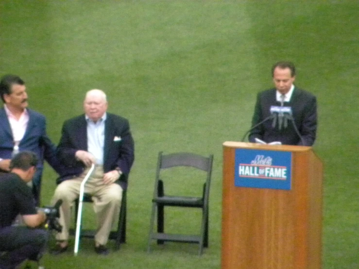 two men sitting in a stadium are standing next to a microphone and two people sitting on chairs