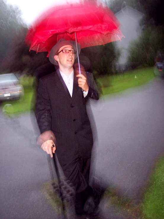 a man wearing glasses is walking on the street holding an umbrella