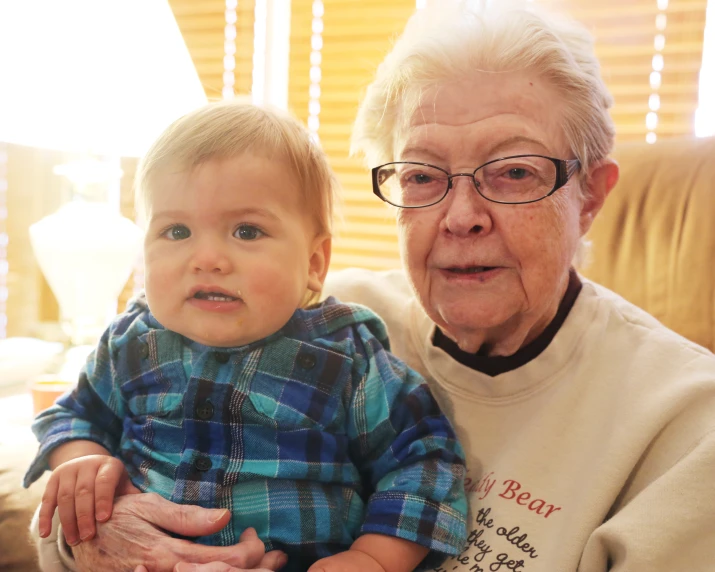 a toddler wearing glasses is in the lap of an elderly person