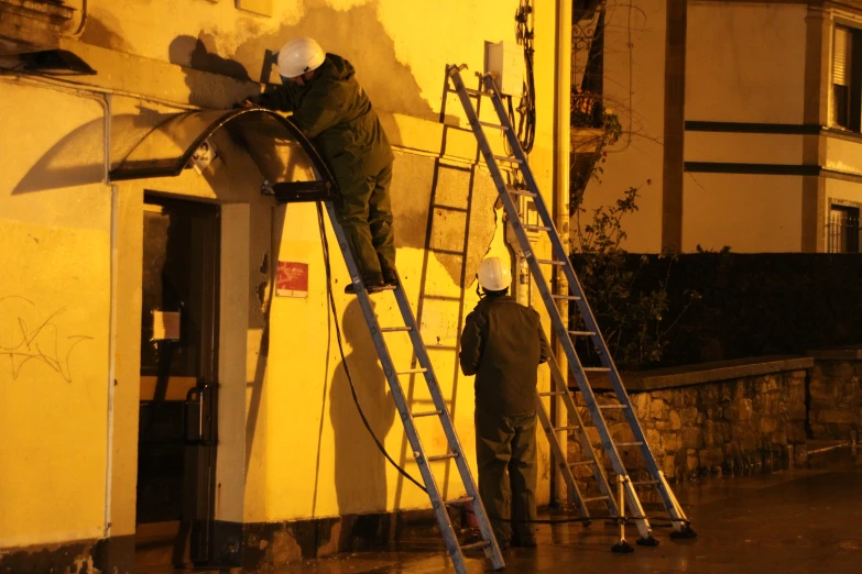 two people working on the side of a building with their hands in paint