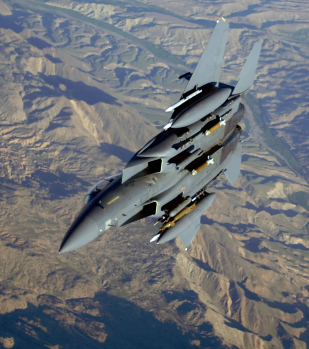 a fighter jet flies high over a land covered with hills