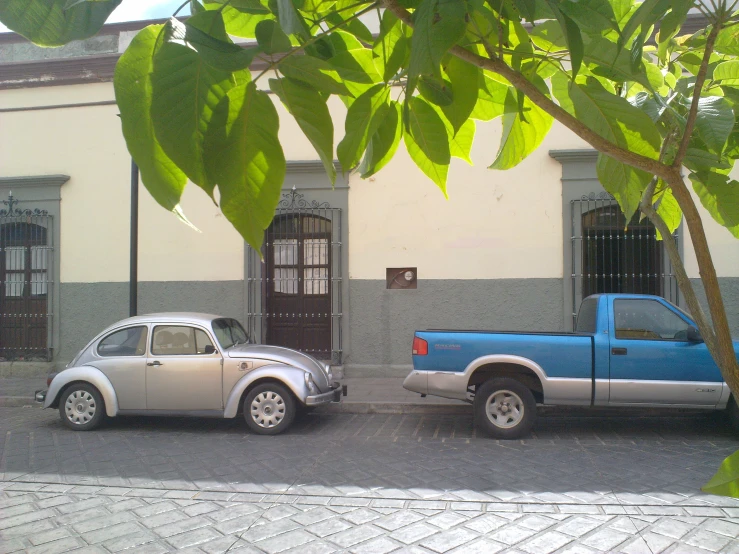 a blue truck next to a grey car on a cobblestone driveway