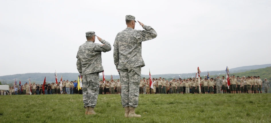 two soldiers salute while a group of people watch