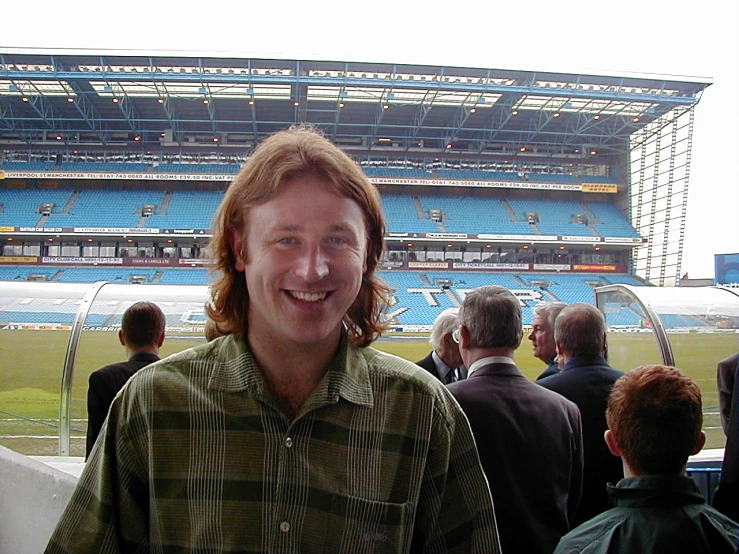 man smiling in front of arena with several people