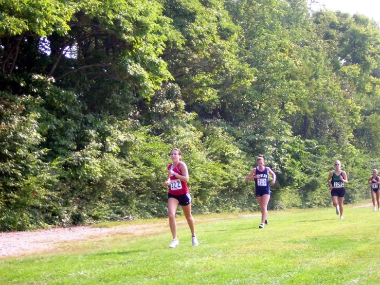 a group of people running through a grass covered field