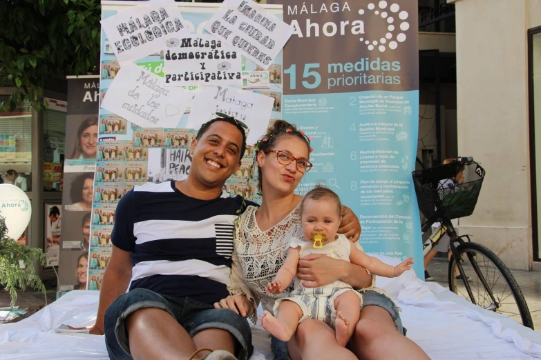 a man and woman holding a baby with posters on the background