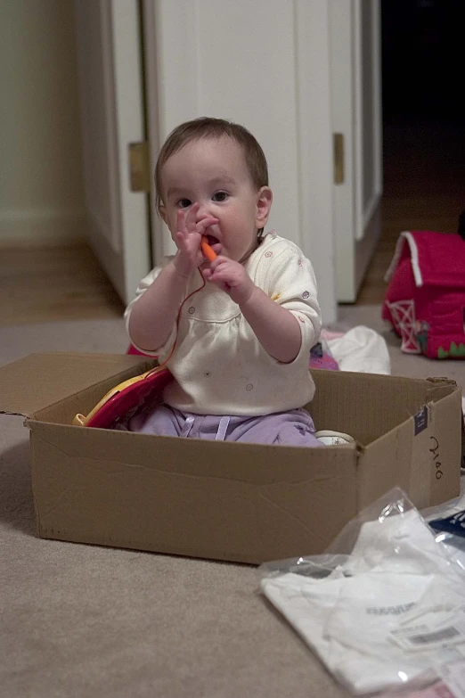 a baby sitting in a box eating a carrot