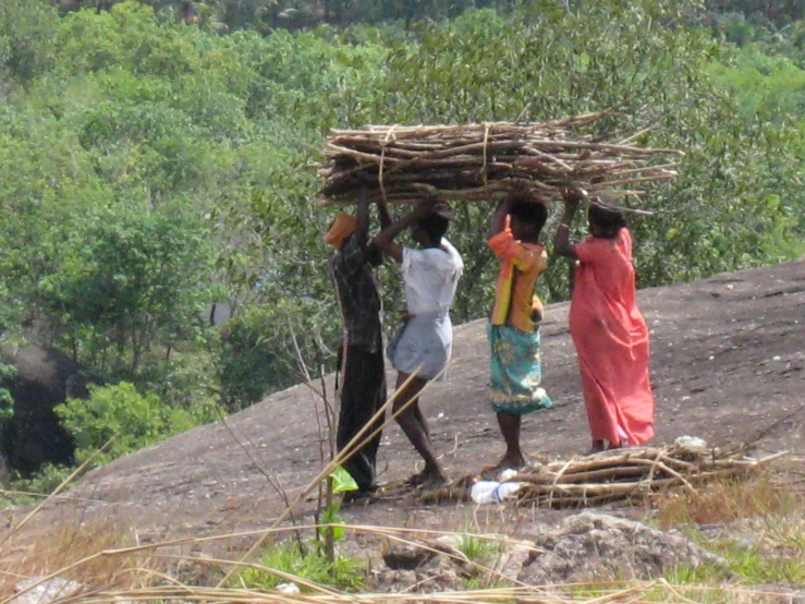 three children carrying baskets over their head while standing near a hill