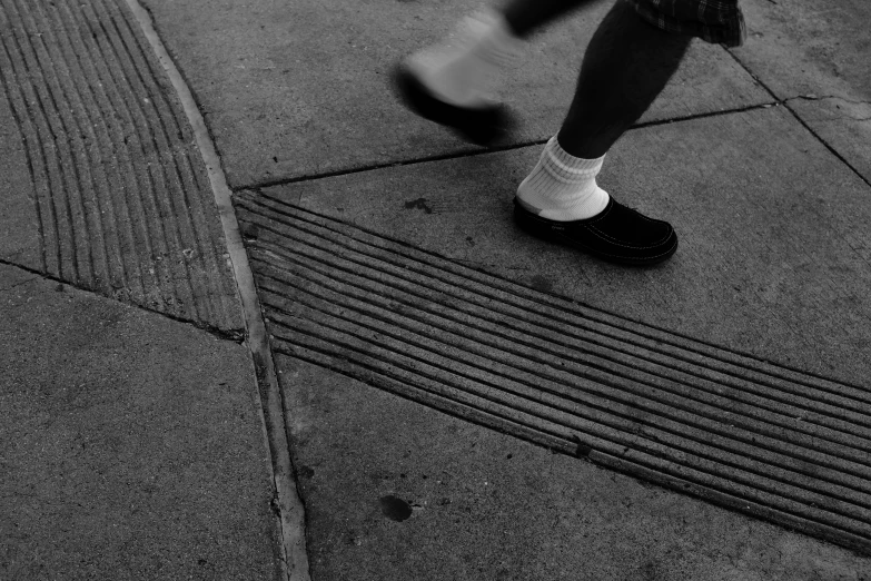 black and white pograph of person's legs on the sidewalk