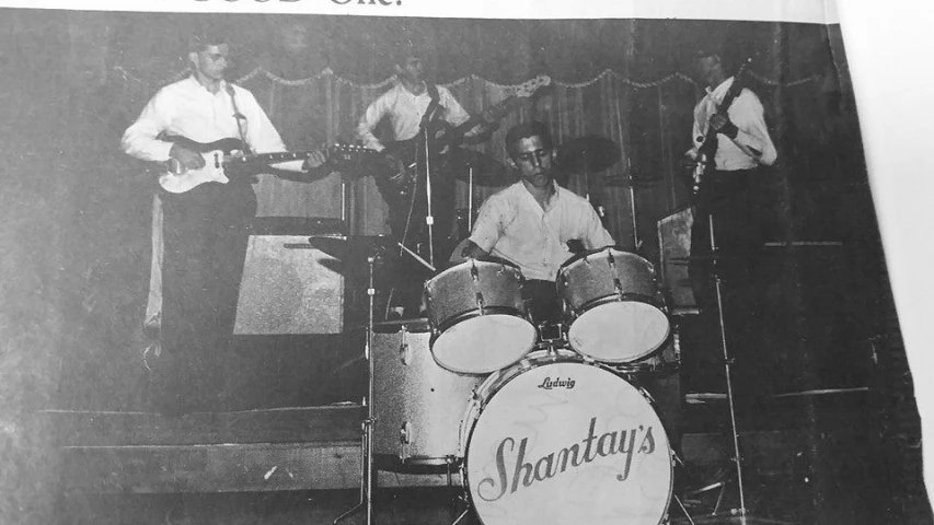 two men and a girl playing instruments in front of a band