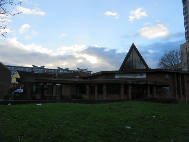 the building in front of the green field has a few birds flying