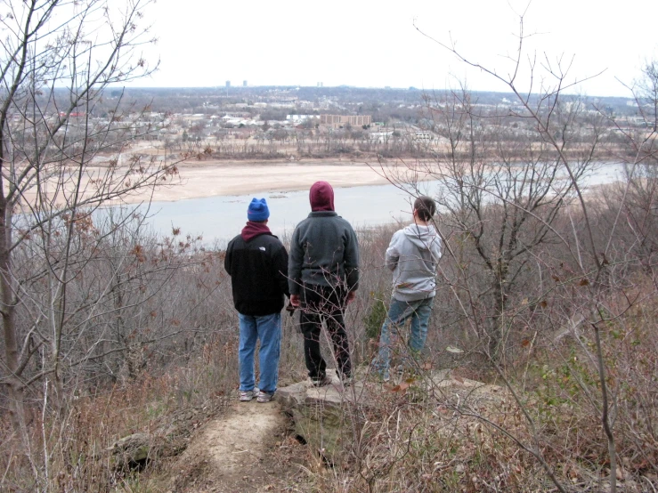 four people stand on the edge of a trail near some water