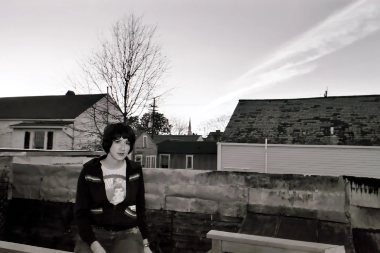 a woman is posing on a ledge near a house