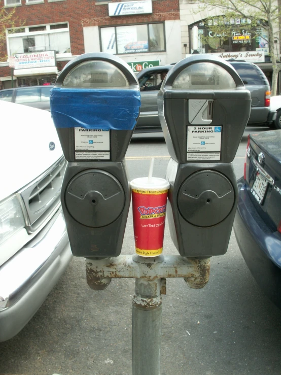 two parking meters on top of a pole near parked cars