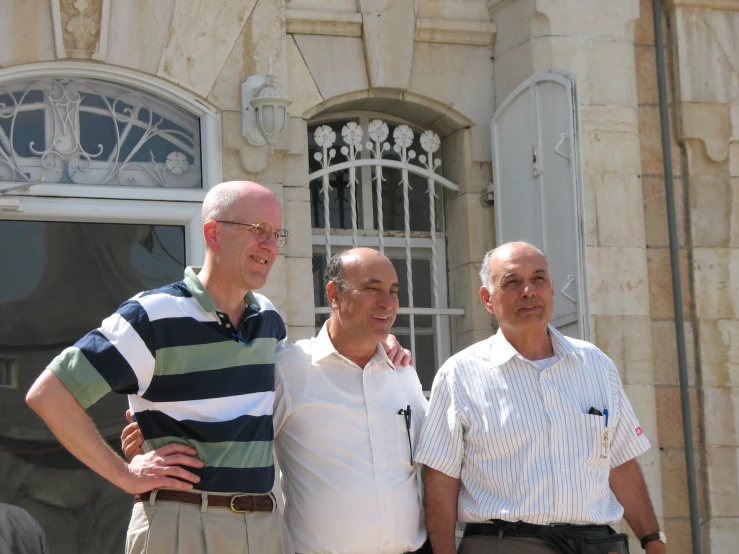 three men pose for the camera in front of a window