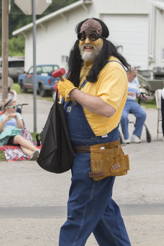 man with painted facial and face mask in overalls walking with bag