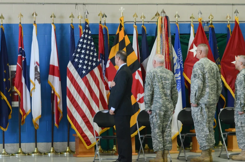 two people in uniform saluting at men and women standing around several flags