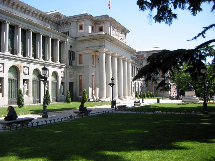 a grassy lawn with benches around it and large white building behind