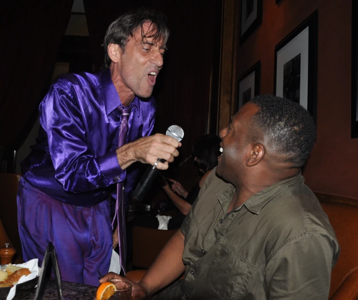 two men sitting at a table and one is holding a microphone