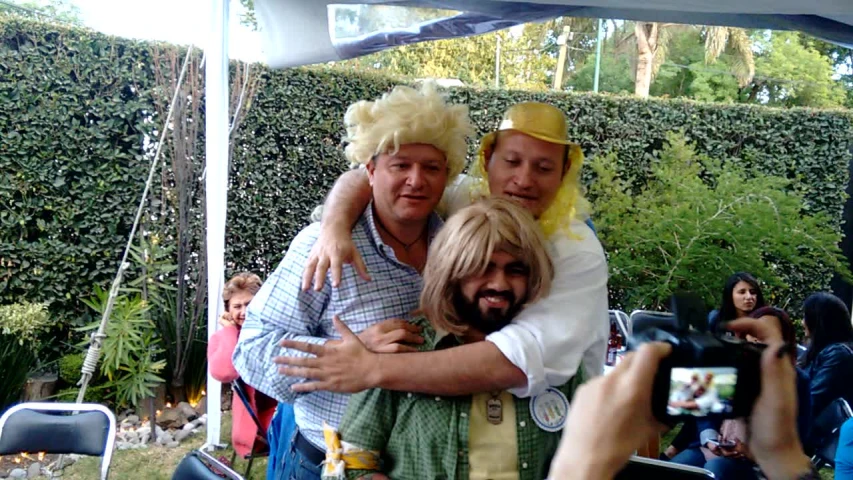 two men, one of them in a wig hugging and laughing with each other
