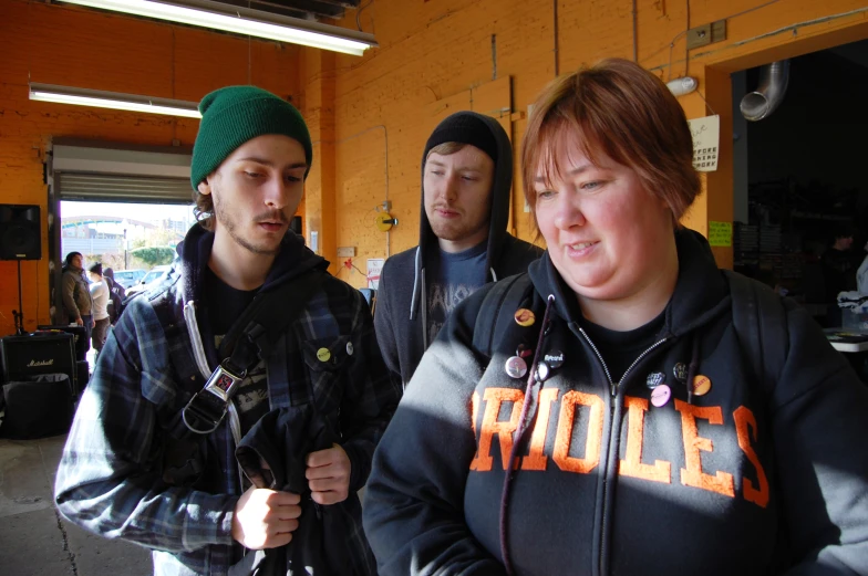 two men in a building looking at a woman in a hat and a sweater