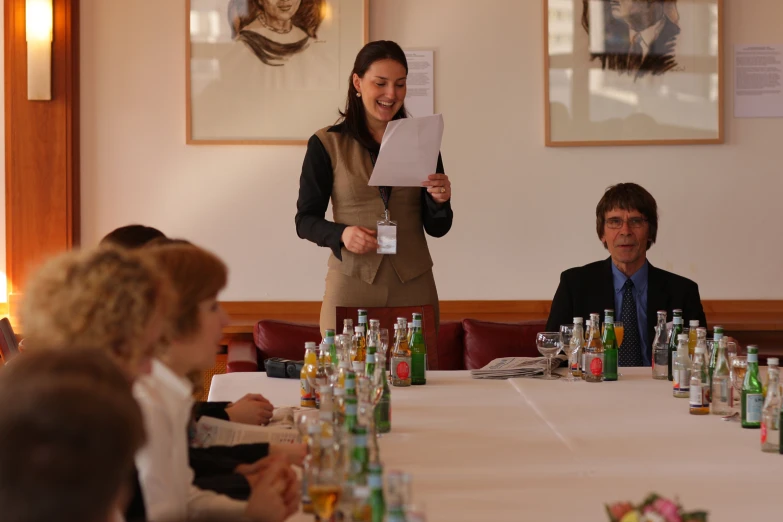 a woman holding up her papers over her right shoulder while standing behind a table full of people