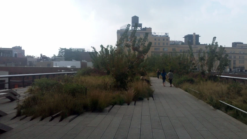 two people are walking along a boardwalk near tall buildings