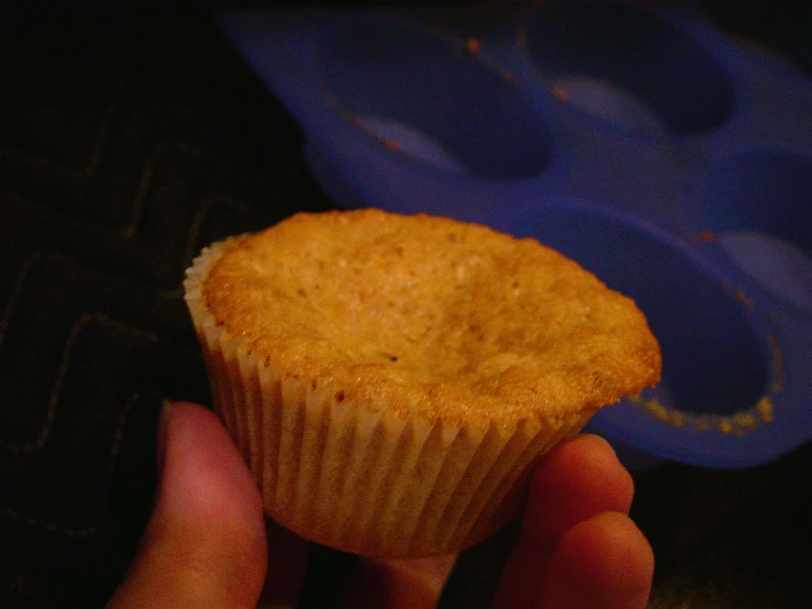 a hand holding a cup cake with a muffin topping on top