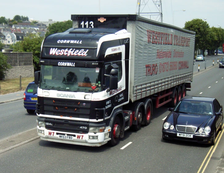 a car passes a large semi truck with a flat bed trailer