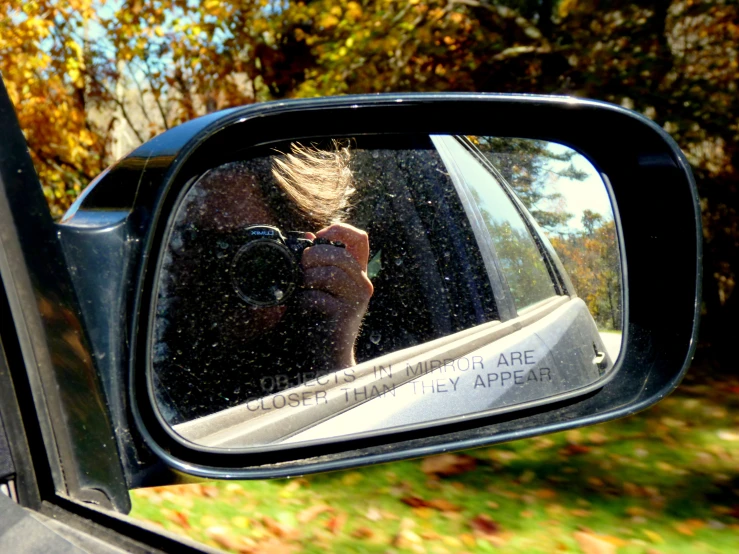 the side view mirror of a car reflects a woman's reflection in her sunglasses