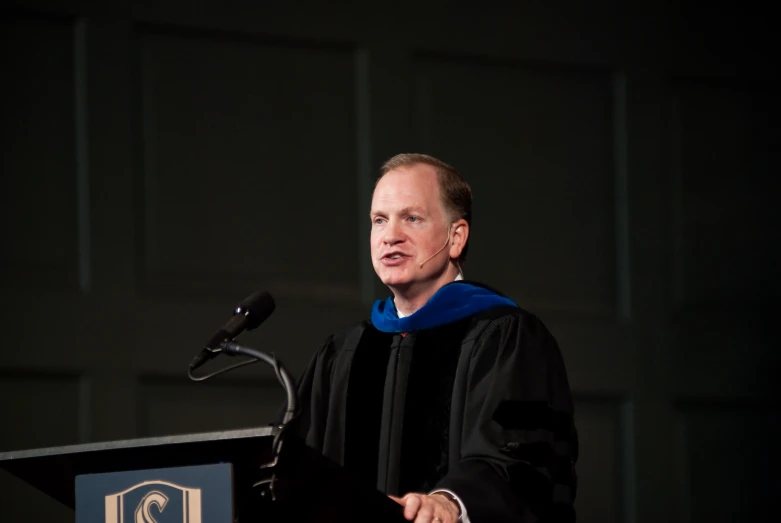 a man in his graduation gown speaking at a podium