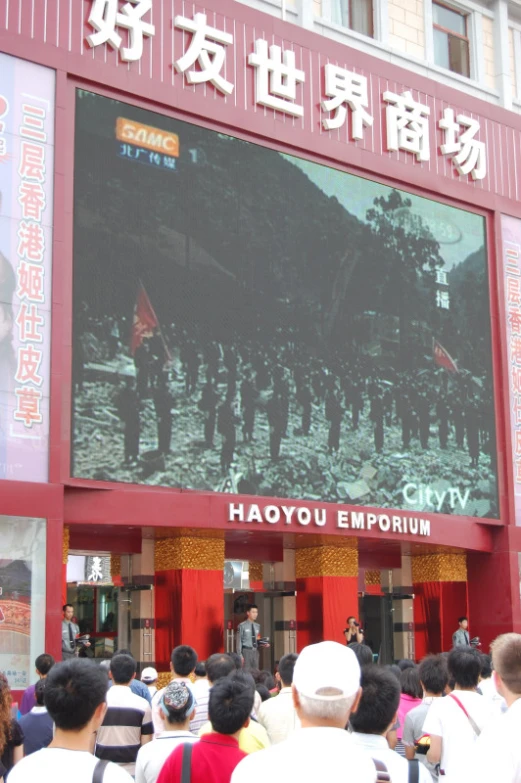 people standing outside of a building, watching a display showing military men on the side