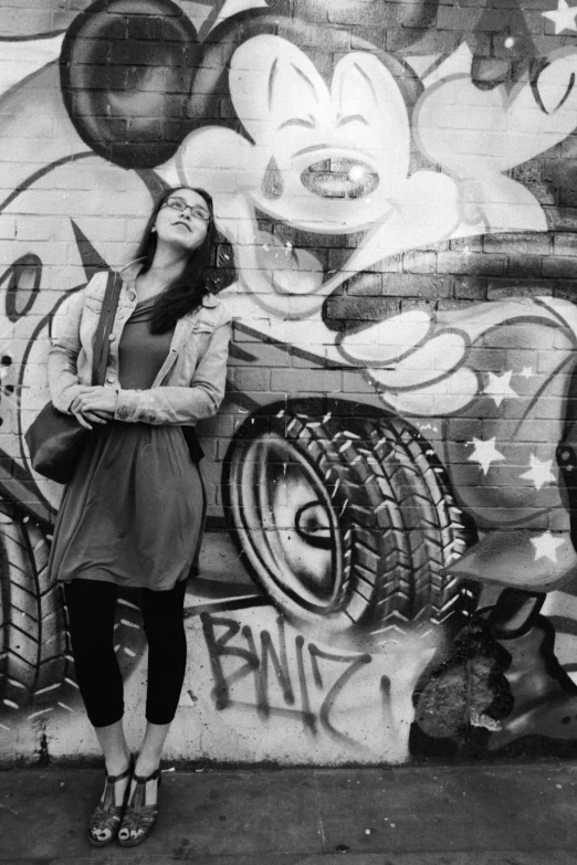 the woman stands near a wall with a mural of a car