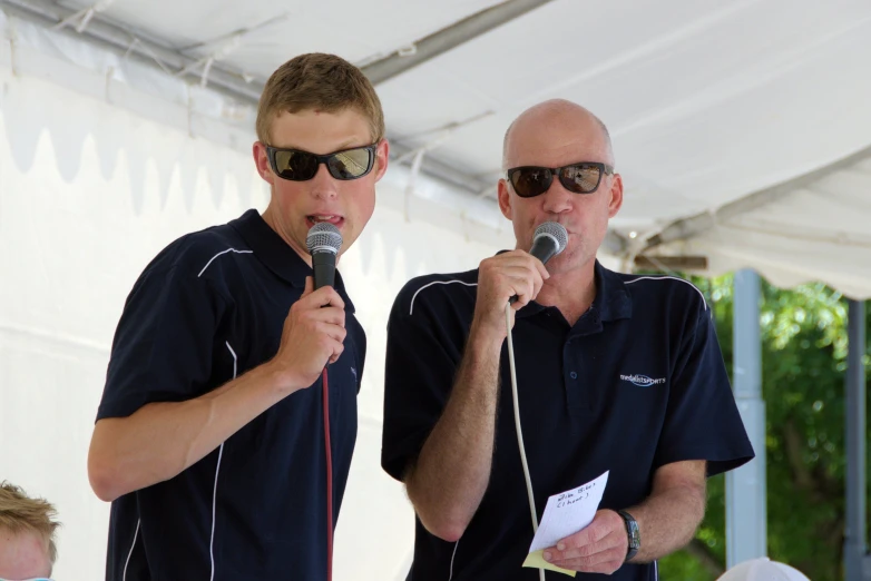 two men stand with microphones and listen to each other