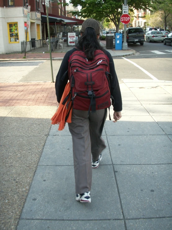 the woman walks down the sidewalk with a backpack