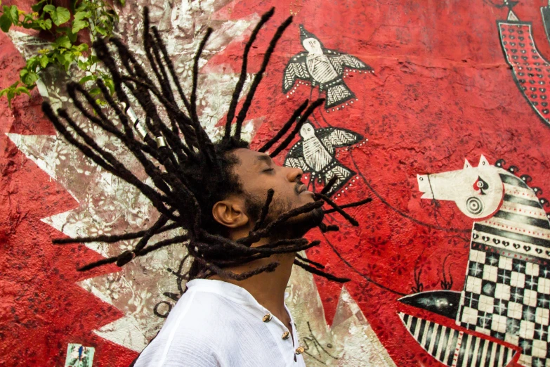 a person wearing dreadlocks and looking up at a wall with a colorful painting