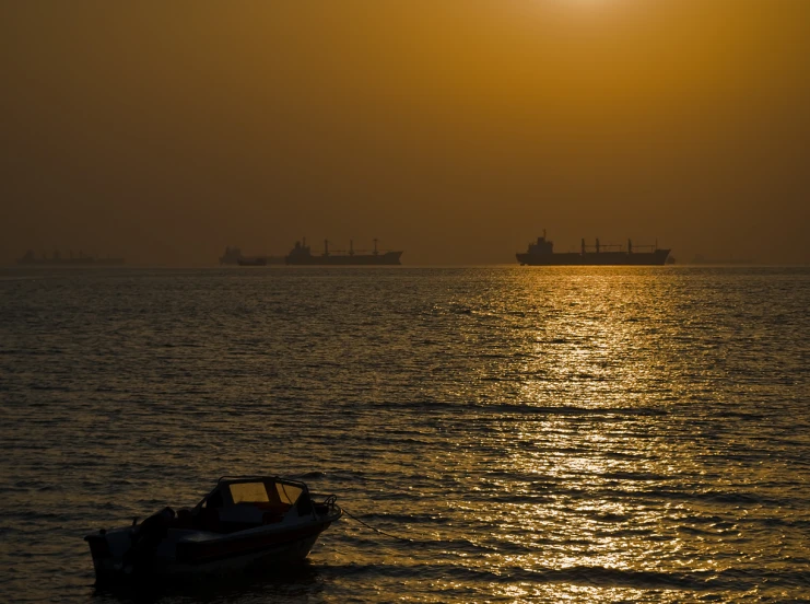 a small boat sits out on a lake as two large ships are in the distance