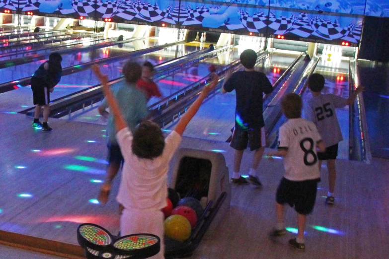 a group of young people with their arms raised at the bowling alley