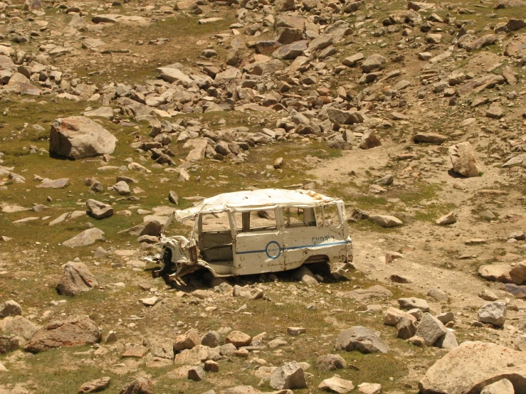 an old vehicle sitting on rocks with a rock field below