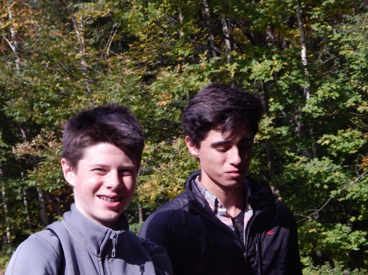 two young men standing in the woods next to trees