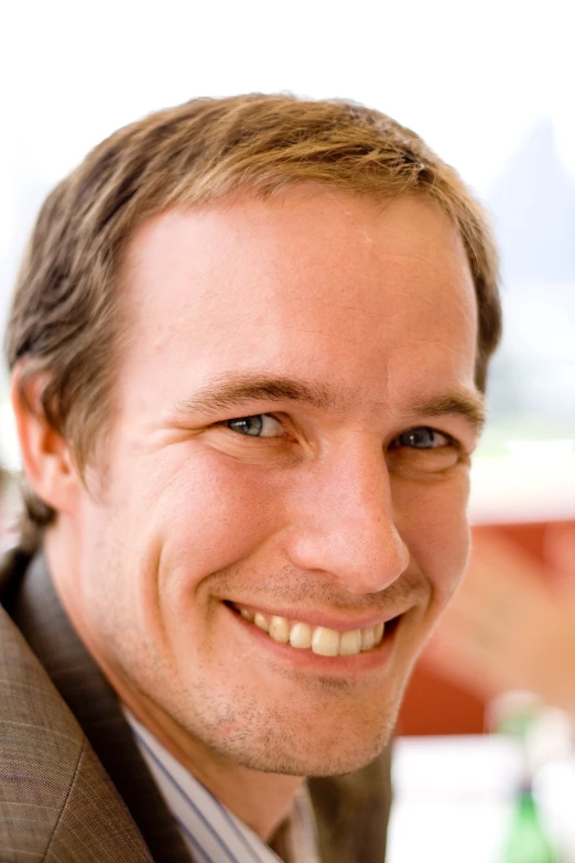 a man smiling for the camera with a tan jacket on