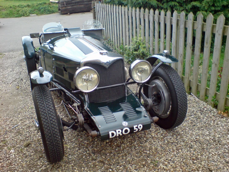 an old fashioned car sitting in front of a fence