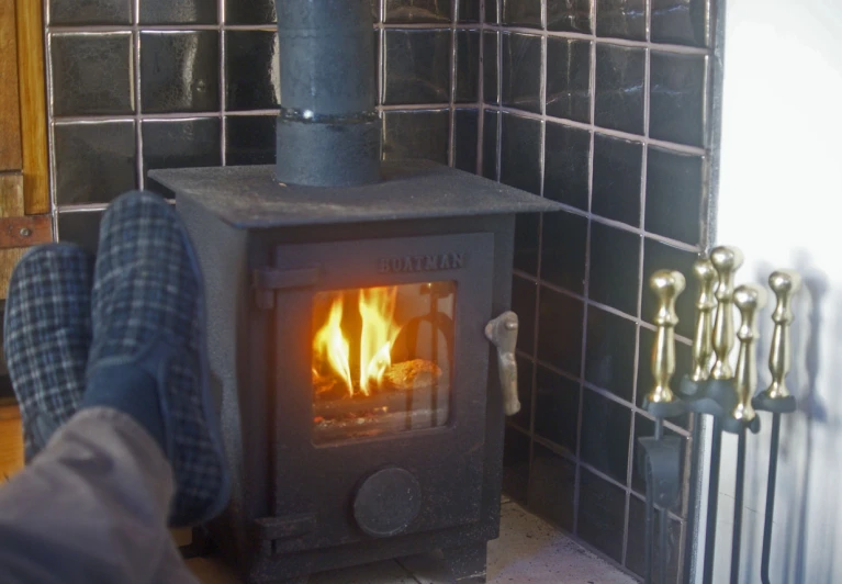 a person in blue checkered pants stands by a fire