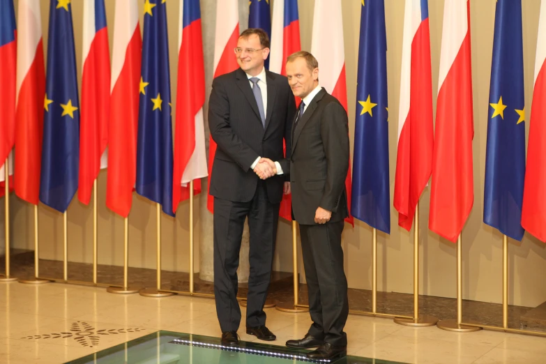 two men in suits and ties standing beside flags