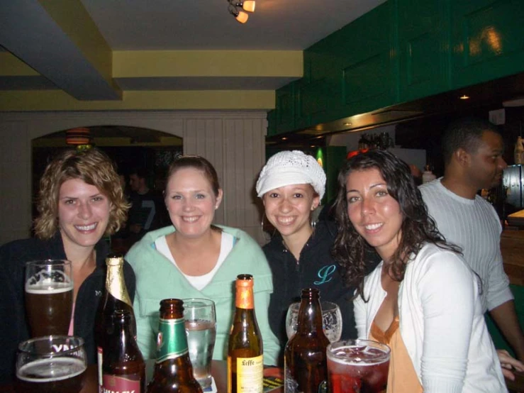 four girls at a bar holding glasses of beer