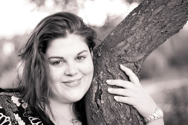 a black and white po of a woman leaning on the side of a tree
