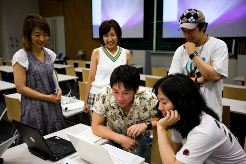 people looking at a laptop computer screen with two of them on a desk