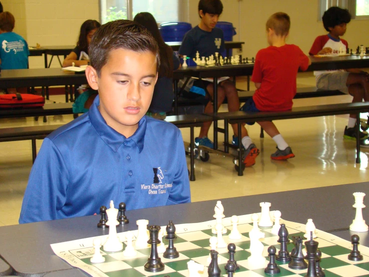 a young man sitting at a table with chess pieces
